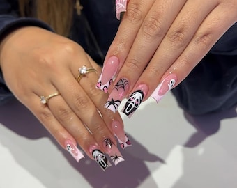 May include: Long, square-shaped acrylic nails with a Halloween theme. The nails feature a pink and white color scheme with spiderwebs, spiders, and a Scream mask design. Some nails have a white ghost design.