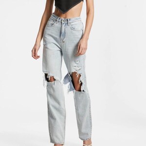 May include: Light wash denim jeans with distressed details, featuring large rips at the knees. The jeans have a classic five-pocket design and a straight leg fit. The light blue colour and ripped details give the jeans a casual, worn look.