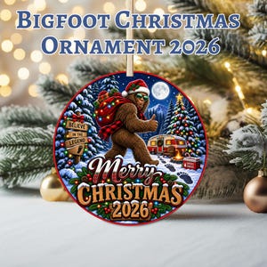 May include: A round Christmas ornament featuring a brown Bigfoot wearing a Santa hat and sunglasses, carrying a red plaid sack. The scene includes a camper, a sign reading Believe in the Legend, and the text Merry Christmas 2026 in a snowy forest.