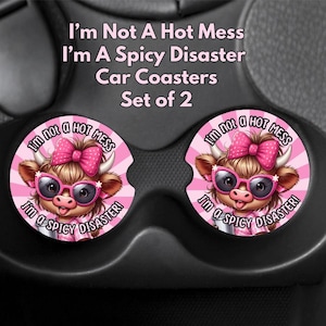 May include: Set of 2 car coasters with a pink and white design. Each coaster features a cartoon cow wearing sunglasses and a bow, with the text "I'm Not A Hot Mess, I'm A Spicy Disaster!"