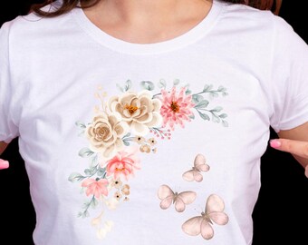 Può includere: T-shirt bianco con un design floreale con accenti rosa, beige e verdi, e tre farfalle. Il design è sulla parte anteriore della maglietta.