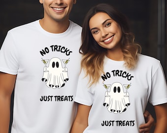 May include: White t-shirts with a Halloween-themed graphic. The design features a cartoon ghost holding martini glasses, with the text "NO TRICKS JUST TREATS" in black. The shirts are worn by a man and a woman.
