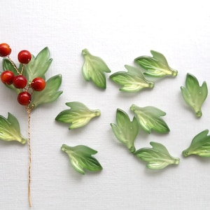 May include: A collection of glass leaves and berries. The leaves are translucent green with yellow highlights, and the berries are small and red. A stem of berries and leaves is on the left, with loose leaves scattered around.