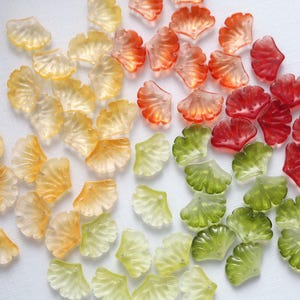 May include: A collection of translucent, fan-shaped beads in various colors, including yellow, orange, red, and green. The beads are arranged on a white surface, showcasing their delicate, petal-like design. These beads are ideal for jewelry making or craft projects.