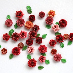 May include: A collection of miniature roses in various shades of red, pink, and gold, scattered on a white surface. The roses are accompanied by small green leaves, creating a floral arrangement.