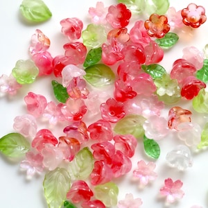 Peut inclure: Un assortiment de perles translucides en forme de fleurs et de feuilles, dans des tons de rose, de rouge et de vert. Les perles sont dispersées, créant une esthétique délicate et fantaisiste. Idéal pour la création de bijoux et l'artisanat.