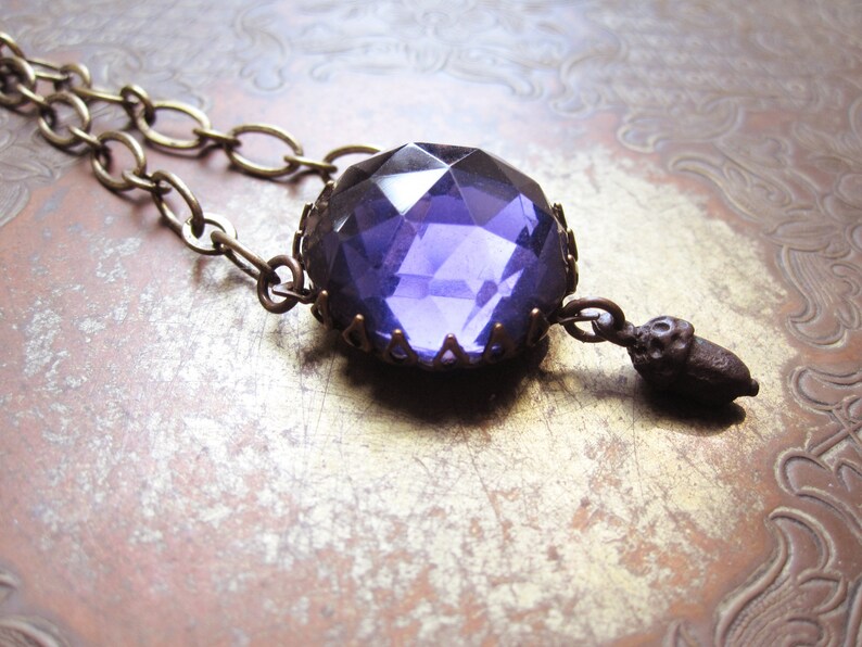 May include: A purple glass pendant necklace with a bronze chain and an acorn charm.