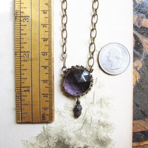 May include: A purple glass pendant necklace with a brass chain and an acorn charm. The pendant is faceted and has a geometric design. The necklace is approximately 18 inches long.