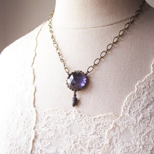 May include: A necklace featuring a large, faceted, dark purple gemstone pendant. The pendant is attached to a gold chain.