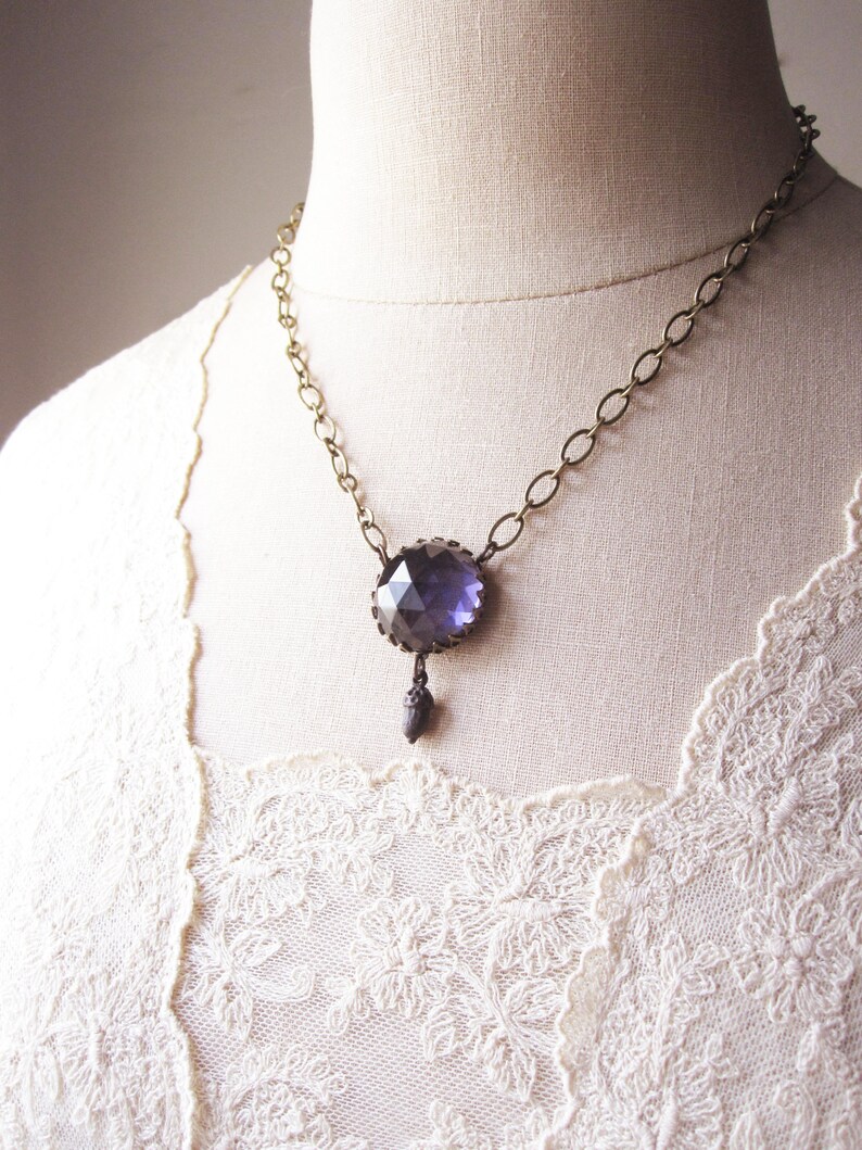 May include: A necklace featuring a large, faceted, dark purple gemstone pendant. The pendant is attached to a gold chain.