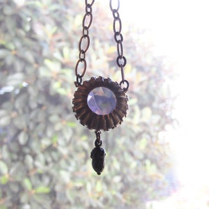 May include: A silver chain necklace with a large, faceted, purple crystal pendant. The pendant is surrounded by a decorative metal frame.