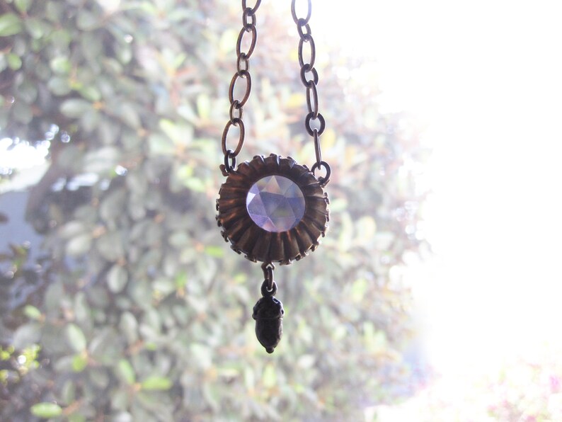 May include: A silver chain necklace with a large, faceted, purple crystal pendant. The pendant is surrounded by a decorative metal frame.