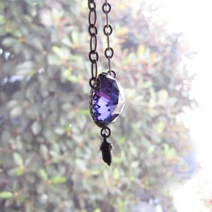 May include: A purple crystal pendant necklace with a silver chain and a small acorn charm.