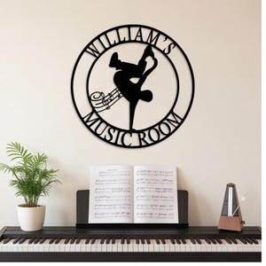 May include: A circular black metal wall sign featuring a silhouette of a person performing a handstand, musical notes, and the text "WILLIAM'S MUSIC ROOM" integrated into the frame. The design is centered and cut from a single piece of material.