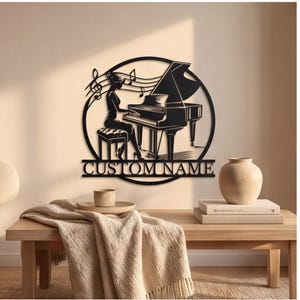 May include: A black metal wall art piece featuring a circular frame with a silhouette of a person playing a grand piano, musical notes, and a horizontal bar at the bottom with the text CUSTOM NAME in a bold, capitalized, sans-serif font.