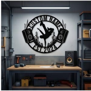 May include: A circular black metal wall sign featuring a silhouette of a person breakdancing in the center, flanked by two speakers and lightning bolts. The text CUSTOM NAME is arched at the top, and EST. 2024 is arched at the bottom.