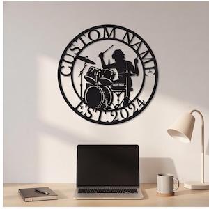May include: A circular black metal wall sign featuring a silhouette of a drummer playing a drum kit. The text CUSTOM NAME is arched across the top, and EST. 2024 is arched across the bottom of the circular frame.