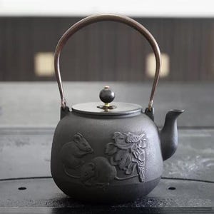 以下が含まれることがあります： 黒い鋳鉄製のティーポット。曲線的なハンドルと小さな注ぎ口が付いています。 ティーポットには、ネズミと花の模様のエンボス加工が施されています。 蓋はシルバーで、小さな黒いノブが付いています。