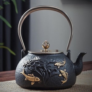 May include: Black cast iron teapot with a silver handle and lid. The teapot features gold koi fish and lotus flower designs. The spout is on the right side, and the lid has a decorative knob.