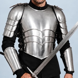 May include: A polished steel breastplate with matching shoulder pauldrons and forearm bracers worn over a black long-sleeved shirt and black trousers. A long, double-edged steel sword with a crossguard and a round pommel is held in the right hand.