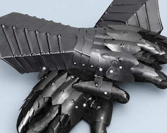 Könnte beinhalten: Ein Paar bewegliche schwarze Metallhandschuhe mit überlappenden Platten, die Unterarm, Handgelenk und Finger bedecken. Die Rüstungsteile sind mit kleinen Nieten befestigt und mit einer dunklen Stoffbasis verbunden, was ein geschichtetes Design ergibt.