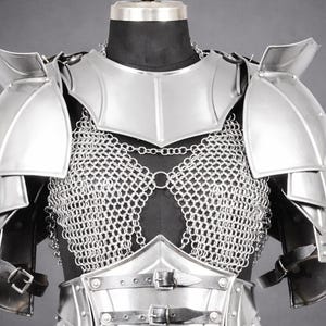 K&ouml;nnte beinhalten: Ein Brust- und Schulterpanzer-Set aus silberfarbenem Metall mit poliertem Brustharnisch, geschichteten Schulterst&uuml;cken und einem Kettenhemd-Oberteil. Die R&uuml;stung verf&uuml;gt &uuml;ber schwarze Lederriemen mit Metallschnallen an Taille und Armen.