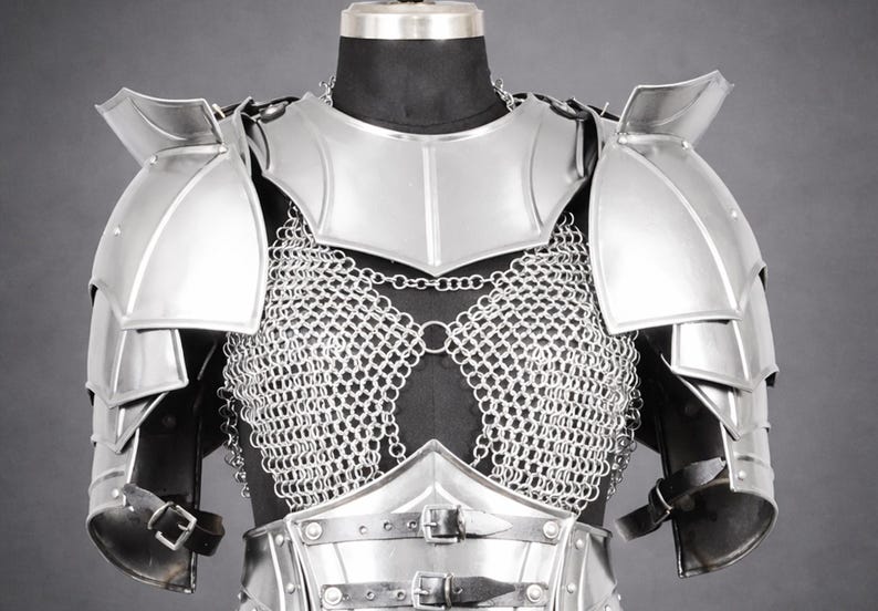 K&ouml;nnte beinhalten: Ein Brust- und Schulterpanzer-Set aus silberfarbenem Metall mit poliertem Brustharnisch, geschichteten Schulterst&uuml;cken und einem Kettenhemd-Oberteil. Die R&uuml;stung verf&uuml;gt &uuml;ber schwarze Lederriemen mit Metallschnallen an Taille und Armen.