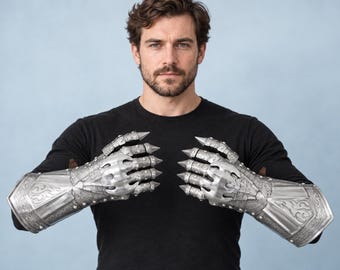 May include: A pair of silver-toned metal gauntlets featuring intricate embossed scrollwork patterns, articulated finger plates, and pointed claw-like tips extending from each finger, covering the hands and forearms in a protective armor style.