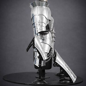 K&ouml;nnte beinhalten: Eine R&uuml;stung aus poliertem silberfarbenem Metall mit beweglichen Schulterst&uuml;cken, einer segmentierten Brustplatte und Kettenhemd-Elementen. Das Set enth&auml;lt passende Armschienen und Beinschienen mit schwarzen Lederriemen und Schnallen.
