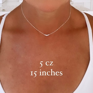 May include: A delicate silver-toned chain necklace featuring five small, clear cubic zirconia stones arranged in a horizontal row at the center. The necklace measures 15 inches in length and includes 5 cz stones as indicated by the text overlay.