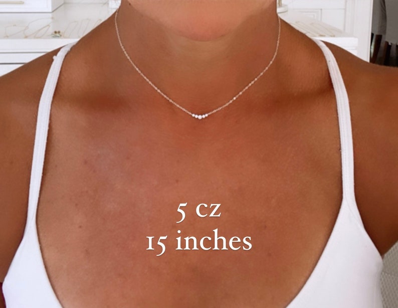 May include: A delicate silver-toned chain necklace featuring five small, clear cubic zirconia stones arranged in a horizontal row at the center. The necklace measures 15 inches in length and includes 5 cz stones as indicated by the text overlay.