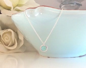 May include: A delicate silver chain necklace with a small, round, light blue gemstone pendant.