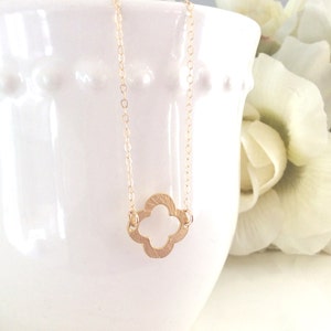 May include: A gold necklace with a delicate, openwork clover pendant. The pendant has a textured, hammered finish.