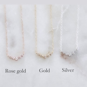 May include: Three delicate necklaces featuring a curved bar of five small round stones. The left necklace is rose gold, the center is gold, and the right is silver. Each necklace has a thin chain and is labeled below as Rose gold, Gold, and Silver.