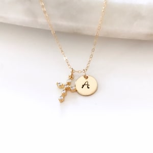 Puede incluir: Collar de oro con un pequeño dije de cruz y un dije redondo con la inicial 'A'.