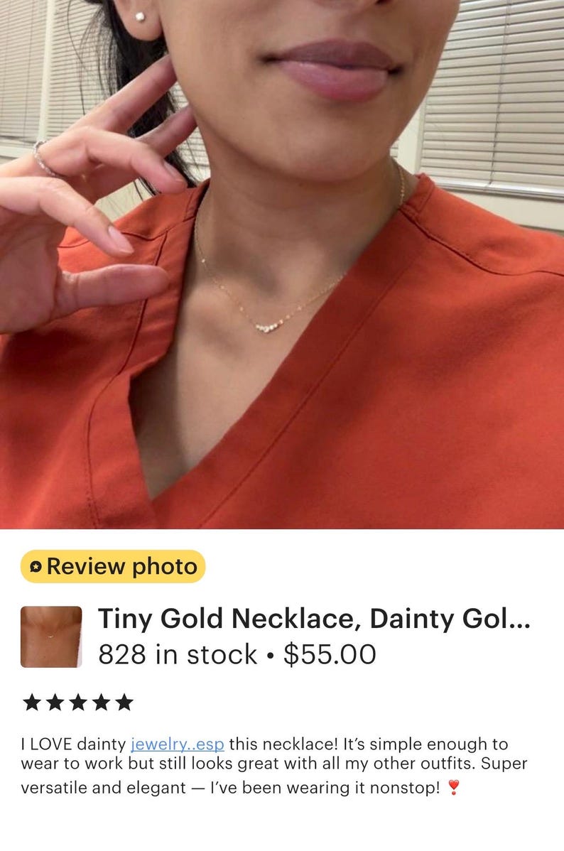 May include: A delicate gold chain necklace featuring a small, curved bar element adorned with five tiny, clear, round-cut stones. The necklace rests against a rust-colored V-neck top, showcasing a minimalist design with a thin, polished metal chain.