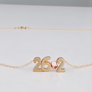 May include: Gold necklace with a pendant featuring the numbers 262. A small rose gold bead separates the numbers.