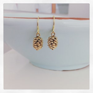Puede incluir: Un par de pendientes de tono dorado con un diseño de piña. Los pendientes son simples y elegantes, perfectos para el uso diario.