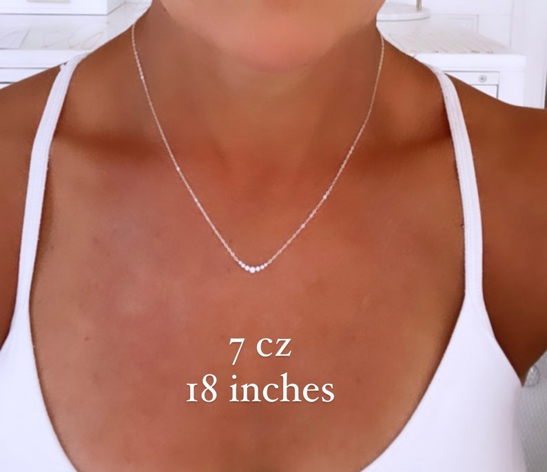 May include: A silver-toned necklace featuring a delicate chain and a central pendant arrangement of seven small cubic zirconia stones. The necklace has a total length of 18 inches and includes 7 cz stones as indicated by the text in the image.