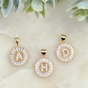 May include: Three gold pendants with a circle of clear cubic zirconia stones surrounding a single letter. The letters are A, D, and H.