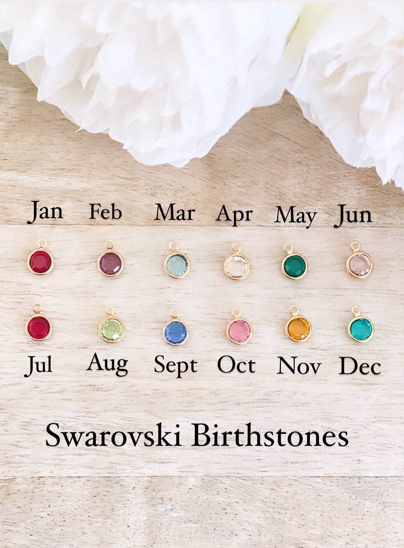 Puede incluir: Doce peque&ntilde;os amuletos redondos con cristales de diferentes colores, que representan las piedras de nacimiento de cada mes del a&ntilde;o. Los amuletos est&aacute;n etiquetados con los meses de enero a diciembre. El texto "Swarovski Birthstones" se muestra debajo de los amuletos.
