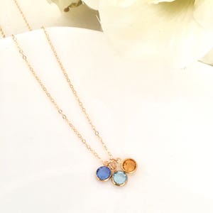 Puede incluir: Un collar de cadena de oro con tres peque&ntilde;os colgantes redondos. Los colgantes son azules, azul claro y naranja.