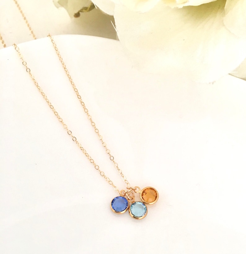 Puede incluir: Un collar de cadena de oro con tres peque&ntilde;os colgantes redondos. Los colgantes son azules, azul claro y naranja.