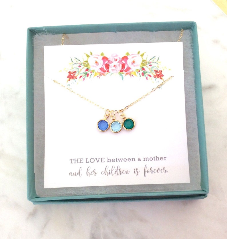 Puede incluir: Un collar de oro con tres peque&ntilde;os colgantes, uno azul claro, uno turquesa y uno verde, en una caja de regalo azul. La caja tiene una tarjeta que dice "El amor entre una madre y sus hijos es para siempre."