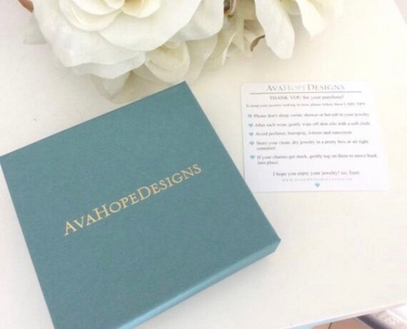 May include: A teal blue box with the text "AvaHopeDesigns" in gold lettering. A white card with the text "AvaHopeDesigns" and care instructions for jewelry.