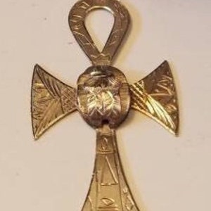 May include: A gold-toned Ankh pendant necklace with intricate details and a cross design. The pendant features a raised, circular design in the center.