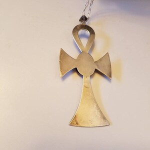 May include: A silver Ankh pendant necklace with a detailed design. The pendant is a cross with a circle in the center and a loop at the top.