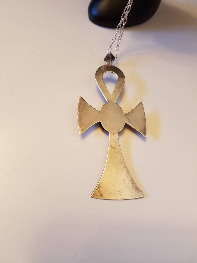 May include: A silver Ankh pendant necklace with a detailed design. The pendant is a cross with a circle in the center and a loop at the top.