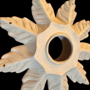 May include: A white ceramic ceiling medallion with a starburst design and eight points. The medallion has a hole in the center and is decorated with a raised feather pattern. The back of the medallion has the text "34720" printed on it.