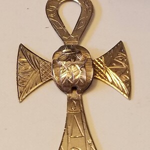May include: A gold-toned Ankh pendant necklace with intricate details and a scarab beetle charm. The pendant is made of metal and has a detailed design.